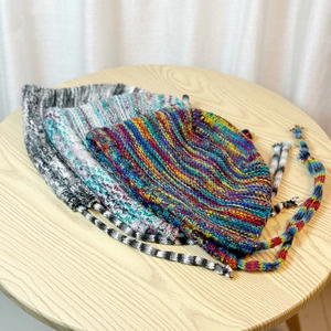 Flat lay of colorful knit earflap beanies on a wooden table with braided straps