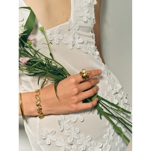 Detail of 18k gold butterfly bracelet and daisy ring worn with a white floral dress