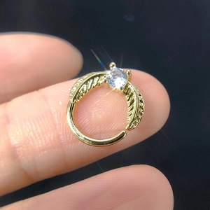 Macro shot of gold zircon nose ring with leaf engraving and clear gemstone on finger