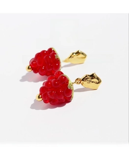Close-up of red raspberry glass earrings with gold leaf detail and cubic zirconia