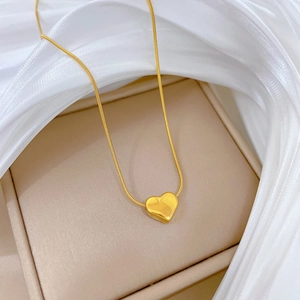 Close-up of gold-plated heart pendant on sleek snake chain over soft silk background