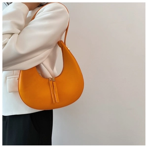 Detail of orange crescent shoulder bag featuring premium leather and double metal zippers
