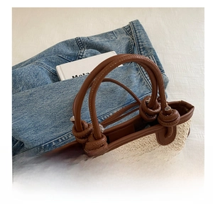 Close-up of a woven straw tote bag featuring brown leather knot handles and metal buckles