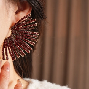 Detail of fan-shaped gold earrings with red rhinestones worn by a model