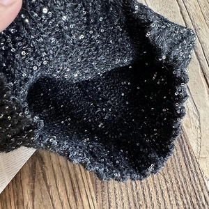 Black knitted sequin beanie hat with silver shimmering details on a wooden background