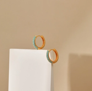 Detail of 18K gold plated hoop earrings featuring turquoise stones on a white geometric stand