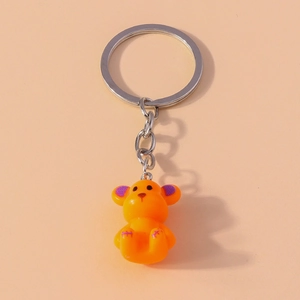 Cute orange bear keychain with purple accents and silver ring on a plain background