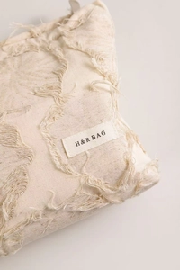 Close-up of beige linen cosmetic bag featuring frayed edges and a H&R BAG woven label