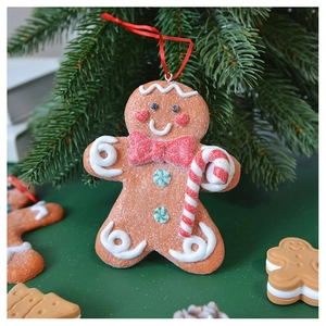 Close-up of gingerbread man ornament with red bow tie hanging on a green Christmas tree