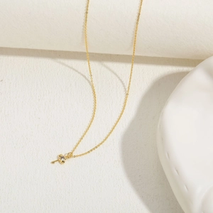 Detailed close-up of a delicate gold key pendant necklace with a round clear zircon stone