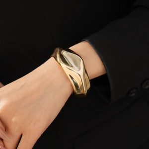 Close-up of minimalist gold folded oval bangle worn with a stylish black suit sleeve