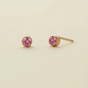 Detail of pink round-cut cubic zirconia studs in gold bezel setting on a beige texture