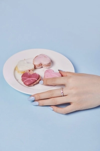 Close-up of a silver ring with pink and purple zircons worn on a hand near macarons
