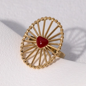 Anello ovale dorato con un cuore di smalto rosso su uno sfondo di pietra bianca