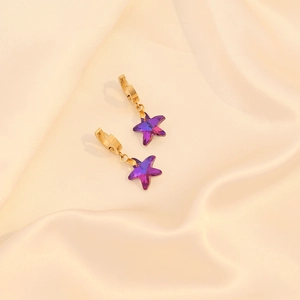 Détail de créoles dorées avec pendentifs étoiles violettes sur tissu de soie beige