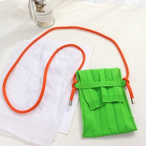Minimalist green knitted mini phone bag with contrasting orange rope strap on white desk