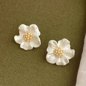 Elegant floral pearl stud earrings with gold accents on a soft green fabric background
