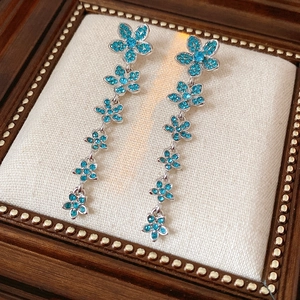Détail de boucles d'oreilles argentées avec cinq pétales de fleurs en zircon bleu en cascade
