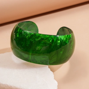 Detail of green marbled acrylic cuff bracelet displayed on a white textured stone