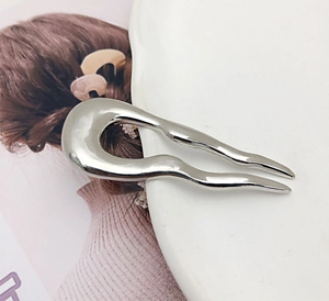 Close-up of a silver irregular U-shaped metal hair fork resting on white porcelain