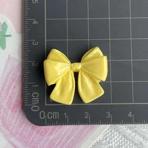 Detailed scale view of a yellow resin bow charm measuring 3cm by 2.5cm on a cutting mat