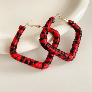Detail of heart-shaped earrings with red and black woven snake pattern and gold hooks