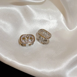 Macro detail of silver V-logo earrings with crystals on white silk background