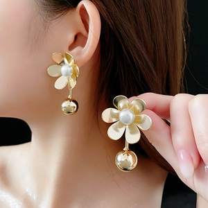 Détail de boucles d'oreilles fleur dorées avec perle blanche et bille métallique