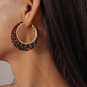 Detailed close-up of a gold-framed resin hoop earring with orange crackle patterns