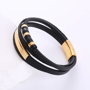 Detail of multi-layer black braided leather bracelet with golden magnetic clasp on rock