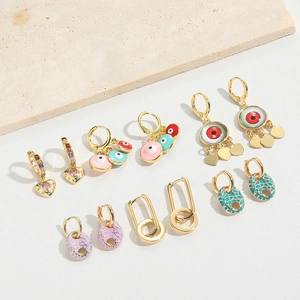 Set of gold earrings with evil eye charms and colorful enamel accents on stone background