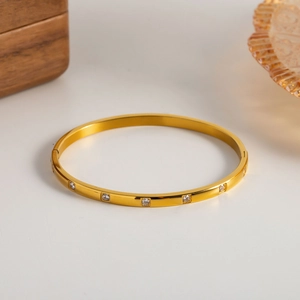 Bracelet jonc en acier plaqué or 18 carats avec zircons blancs sur fond beige