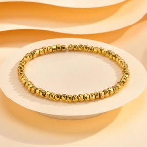 Detail of faceted gold bead bracelet with high-shine metallic finish on white pedestal