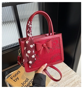 Detail of red bridal handbag with lace embroidery, bow, and silk scarf handle