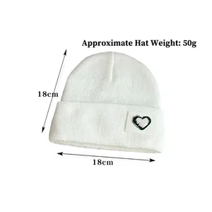 White knit beanie for children featuring a green heart patch and protective ear design