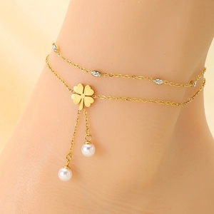 Detail of a double-layered gold anklet featuring a clover and pearls on a model ankle