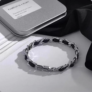 Silver metal and black leather braided bracelet with metal clasp on white book pages