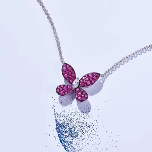 Macro detail of silver butterfly pendant with pink gemstone and zircon on blue sand