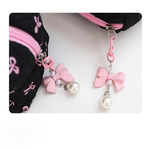 Detail of pink bow and pearl charm on black quilted cosmetic bag with pink zipper