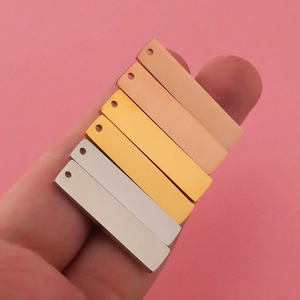 Close-up of three polished rectangular stainless steel pendants in rose gold, gold and silver