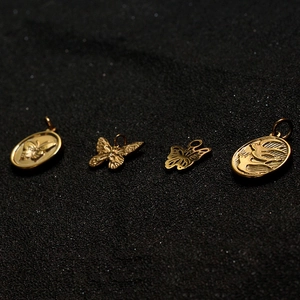 Golden butterfly and oval bird pendants for DIY jewelry making on dark textured background