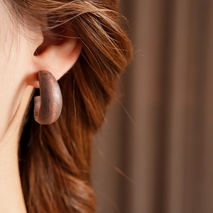 Close-up of a vintage C-shaped dark wood earring with natural grain on a model