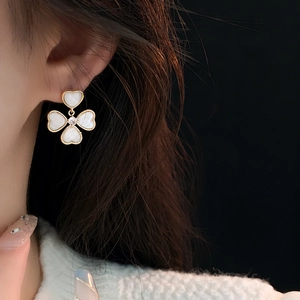 Close-up of elegant gold heart and clover earrings with mother of pearl on model