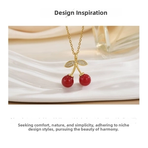 Macro detail of red cherry pendant with sparkling gold leaves and delicate gold chain