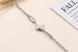 Macro shot of silver cross pendant with elegant oval link chain on a warm beige surface