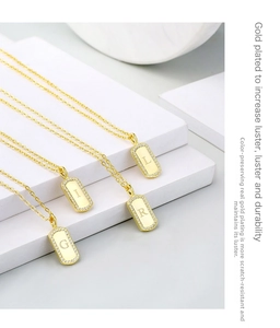Close-up of gold-plated square initial pendants with zircon border on white steps