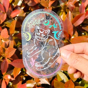 Holographic suncatcher window sticker with cat and moon design held in natural light