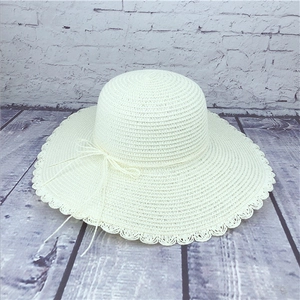 Detailed view of beige straw sun hat featuring elegant scalloped brim and ribbon bow tie