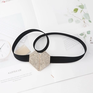 Detail of black elastic belt with a sparkling gold heart-shaped rhinestone buckle