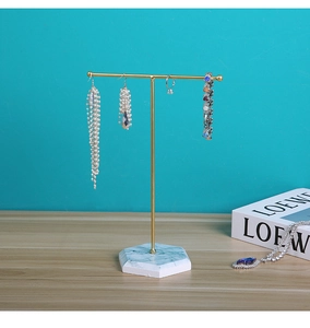 Detail of gold T-bar jewelry stand with a hexagonal marble base on a wooden desk